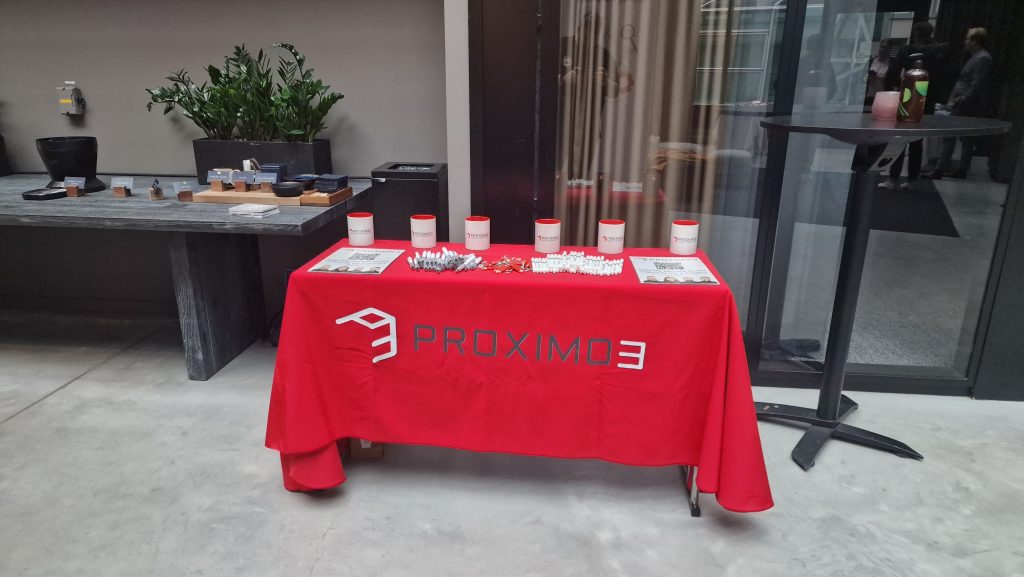 Proximo 3 stand at Nordic Summit with red tablecloth and pens, notepads and mugs on the table