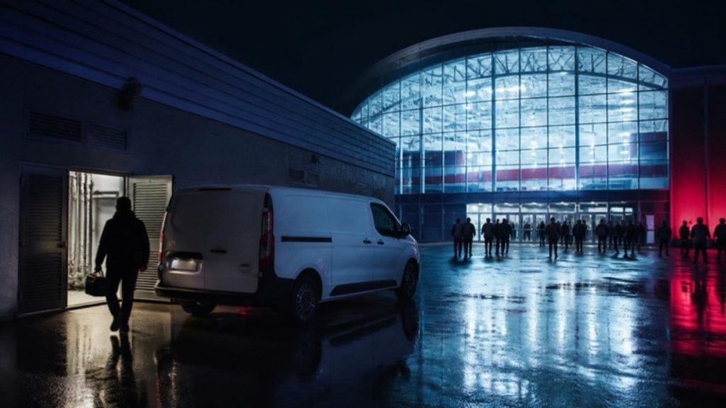 A service van outside an ice arena at night, an engineer heading for the open plant room door